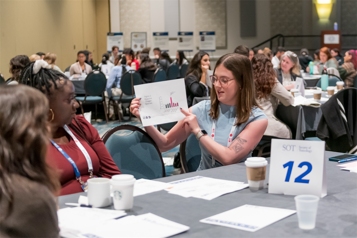 people sitting at a table while one woman holds up a paper